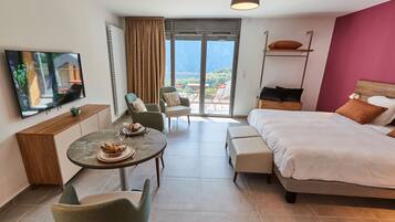 Une chambre d’hôtel moderne équipée d’un lit, d’un coin repas, d’une télévision et d’un balcon offrant une vue sur la montagne.