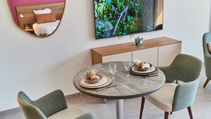 A modern dining area with a round table, two upholstered chairs, a wooden console table, and a flat-screen TV mounted on the wall. - Pure Thermal Résidence (Roquebilliere)