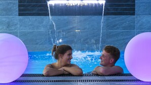 A couple in a pool with a waterfall feature and a tiled wall.