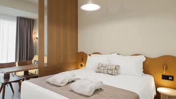 A hotel room with a neatly made bed, a wooden headboard, a bedside table, a desk, and a large mirror.