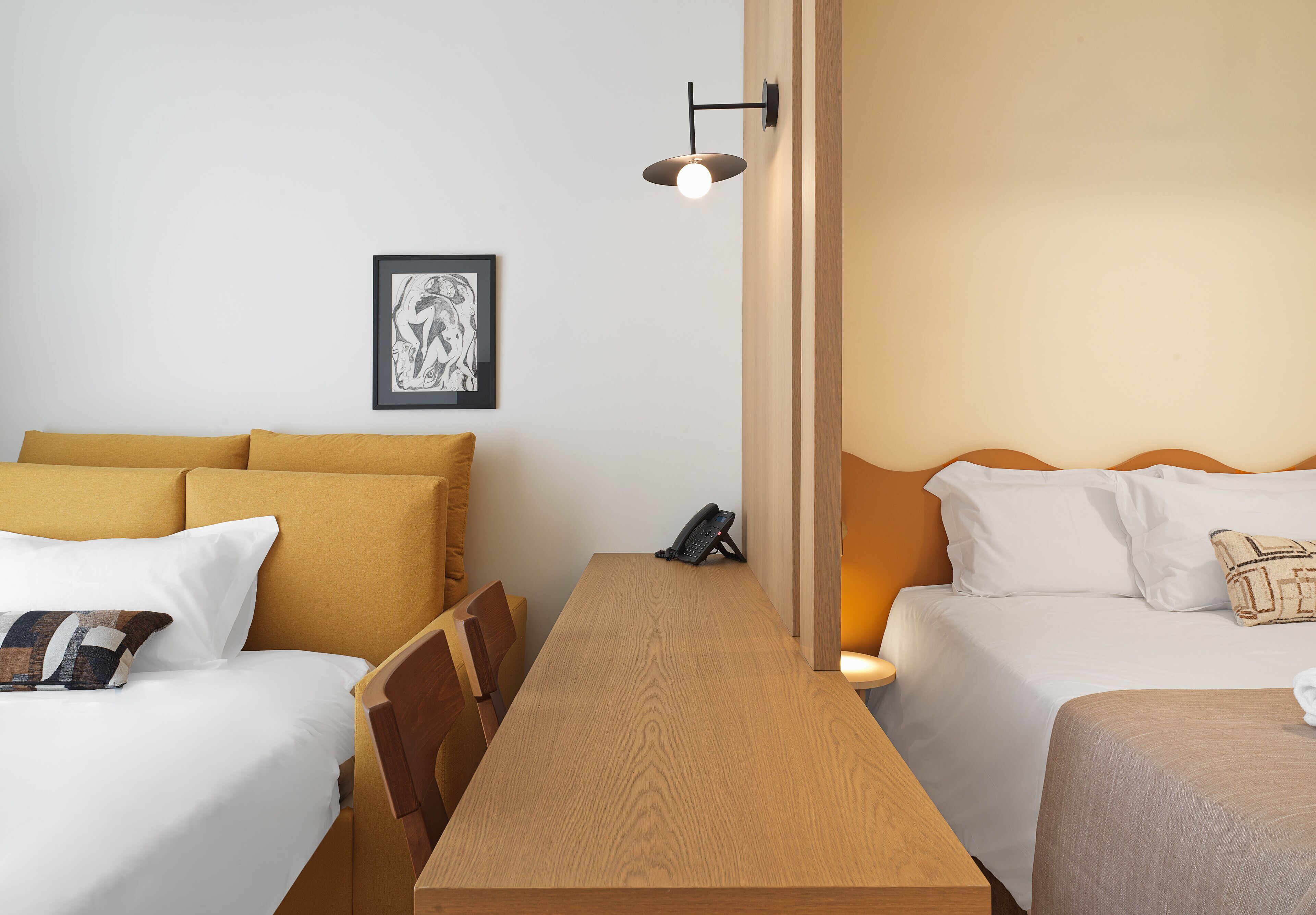 A hotel room with two beds, a wooden table, a framed artwork on the wall, and a phone on the table.