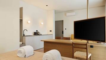 A hotel room with a bed, a desk, a chair, a TV, a kitchen area, and a bathroom.