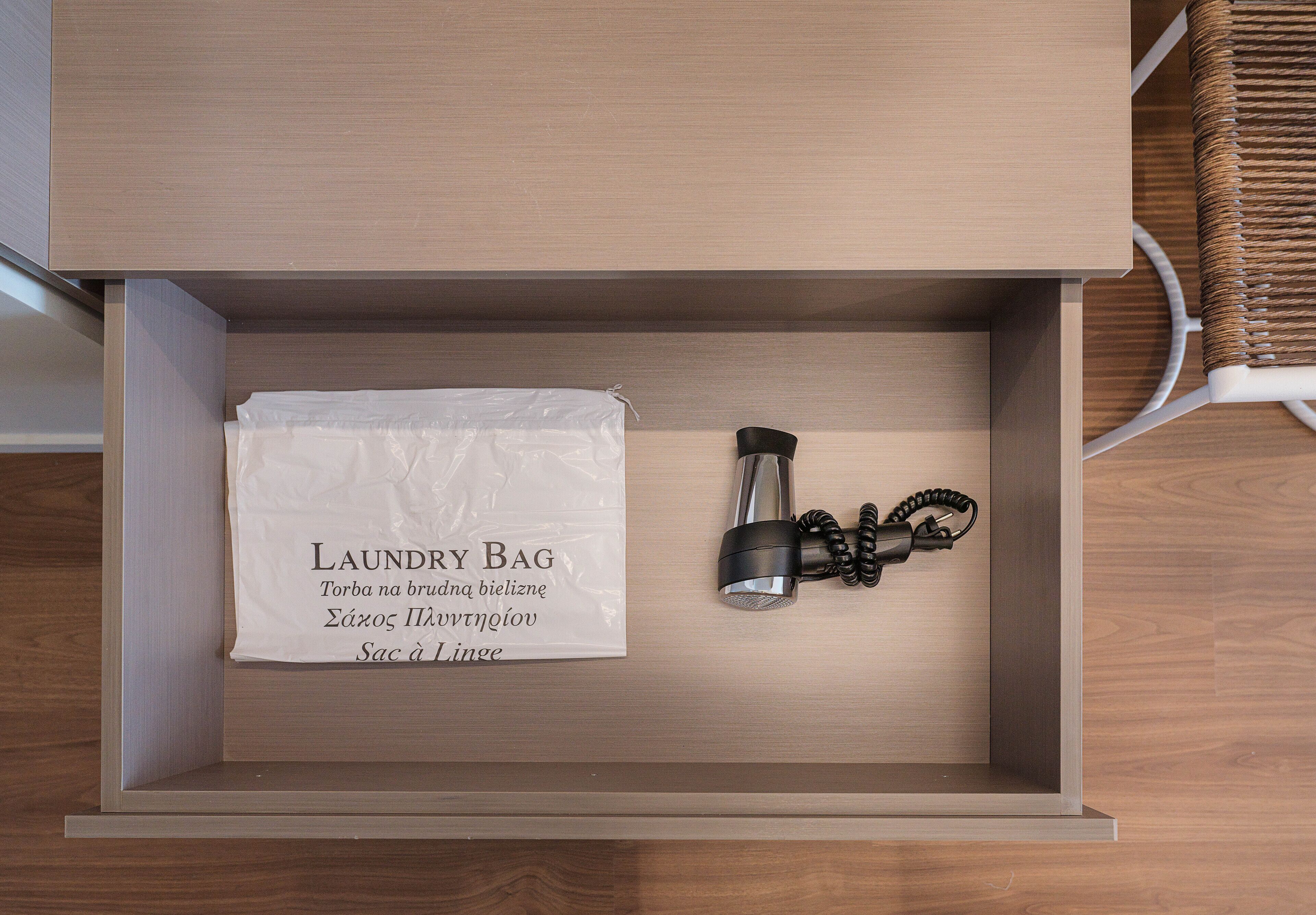 A drawer with a white laundry bag and a black hairdryer.
