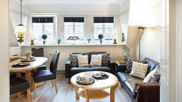 A cozy living room with a round wooden coffee table, a black leather sofa, and a dining table with chairs. - Welcome to the Sylti 3 apartment (List auf Sylt)