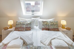 A double bed with white linens, two bedside tables with lamps, patterned pillows, and a window with a view of buildings.