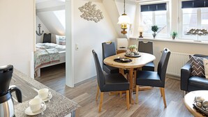A modern kitchen with a dining area, featuring a round wooden table, black chairs, and a coffee maker. - Welcome to the Sylti 3 apartment (List auf Sylt)
