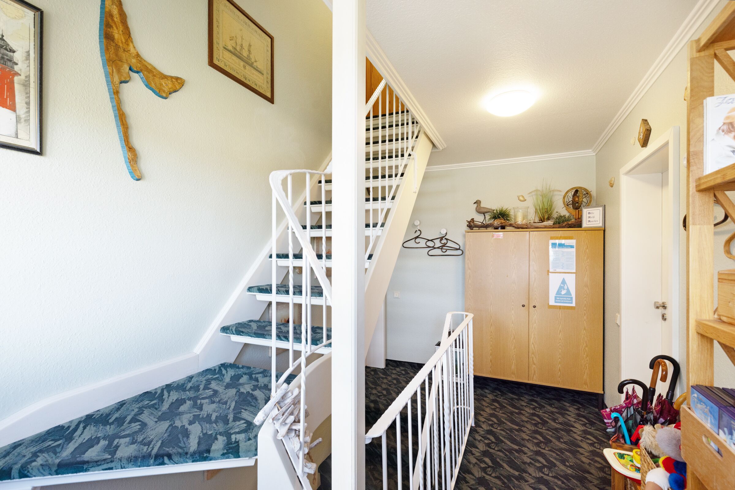 Un escalier avec une rampe blanche, une porte en bois avec une enseigne et une étagère contenant divers objets.