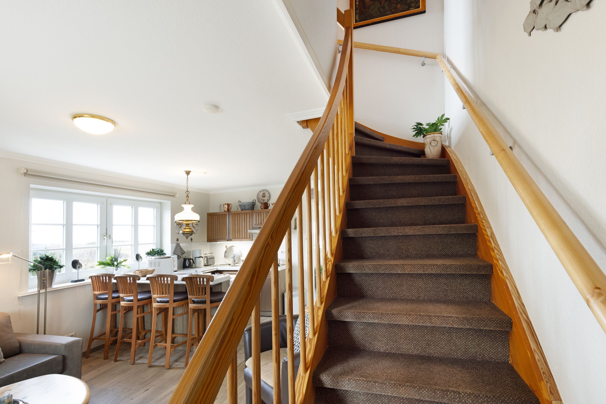 Una escalera con barandillas de madera que conduce a una cocina con taburetes altos y una mesa de comedor.