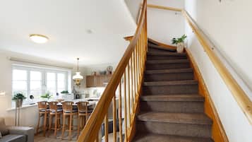 Una escalera con barandillas de madera que conduce a una cocina con taburetes altos y una mesa de comedor.