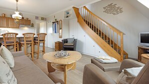 A spacious living room with a wooden staircase, a dining area with wooden chairs, and a cozy seating arrangement.
