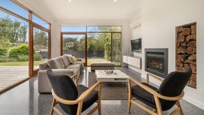 Una sala de estar moderna con sofá, sillas, una mesa de centro, chimenea y un amplio ventanal con vistas al exterior.