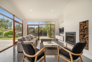 Una sala de estar moderna con sofá, sillas, una mesa de centro, chimenea y un amplio ventanal con vistas al exterior.