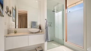 Un baño moderno con cabina de ducha de vidrio, un lavabo blanco y un espejo grande.