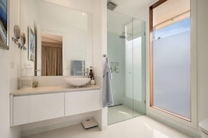 Un baño moderno con cabina de ducha de vidrio, un lavabo blanco y un espejo grande.