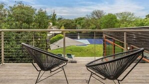 A wooden deck with two black chairs, a pool, and a view of a garden and trees.