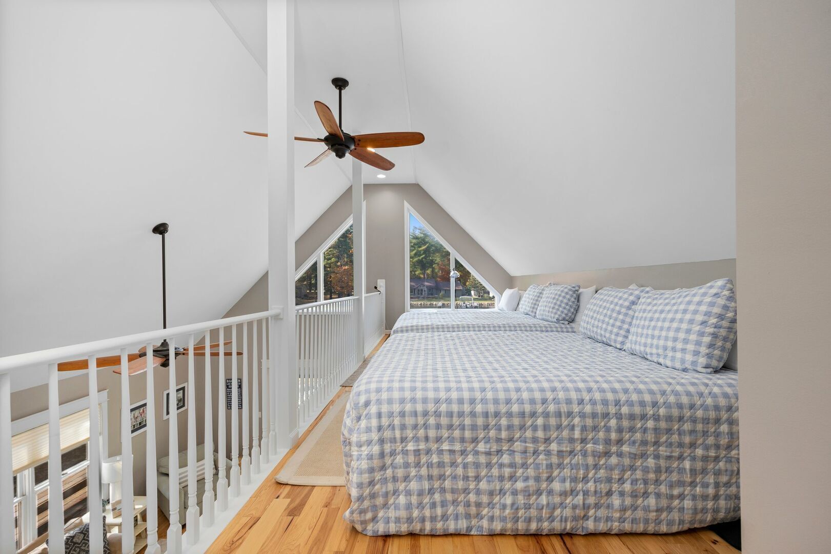 A bedroom with a checkered bedspread, a ceiling fan, and a white railing.