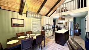 A spacious kitchen with wooden beams, a dining area with a table and chairs, and a living area with a sofa. - 3BDR Home by Torch Lake Sandbar 11931 (Rapid City)