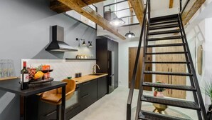 A modern kitchen with a wooden staircase, a black countertop, and a dining area with a chair. - Lumina spacious 2-levels apart (Lódz)