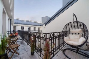 Uma varanda com cadeira de vime, mesa com frutas e bebidas, e plantas em vasos.
