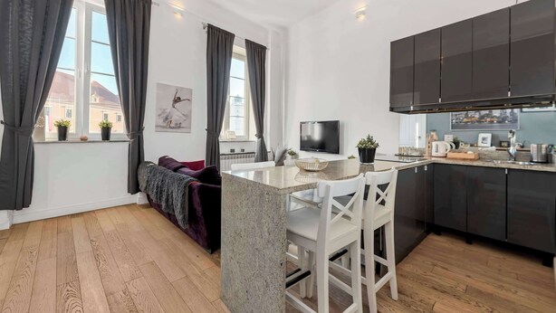 Et moderne køkken med mørke skabe, en central ø og et spiseområde.