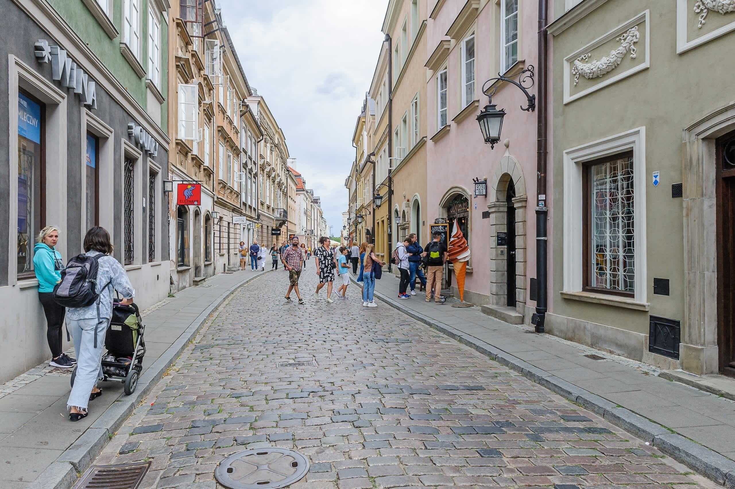 Une rue pavée bordée de bâtiments historiques, une poussette et des piétons.