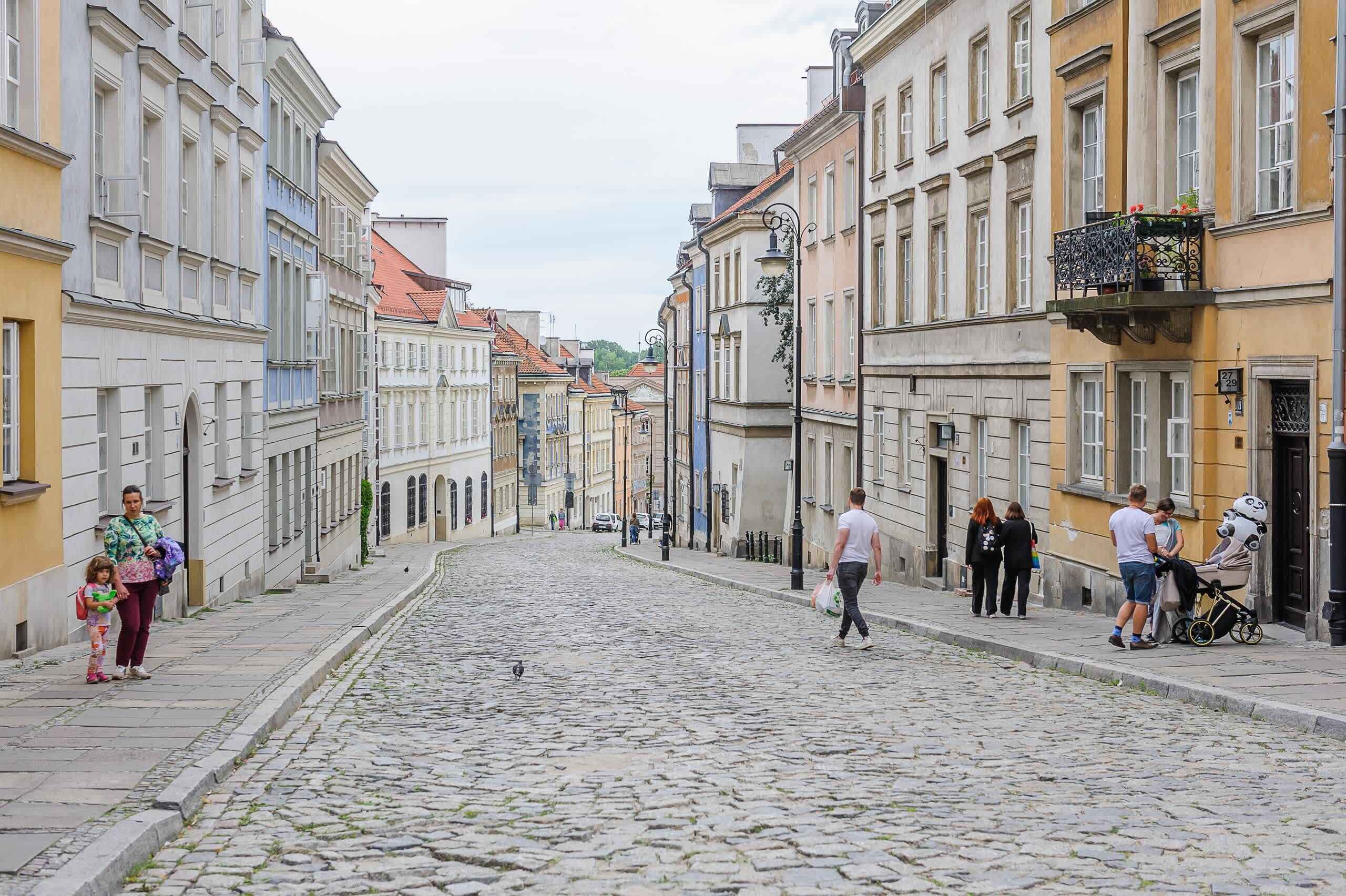 A cobblestone street lined with historic buildings, a stroller, and pedestrians.