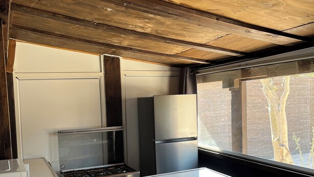 Eine kleine Küche mit einem Gasherd, einem Kühlschrank und einem Fenster mit Blick ins Freie.