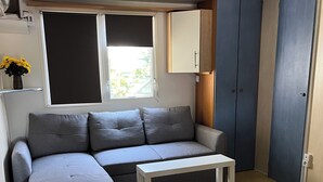 Ein kleiner, moderner Raum mit einem grauen Ecksofa, einem weißen Tisch und einem Kleiderschrank.