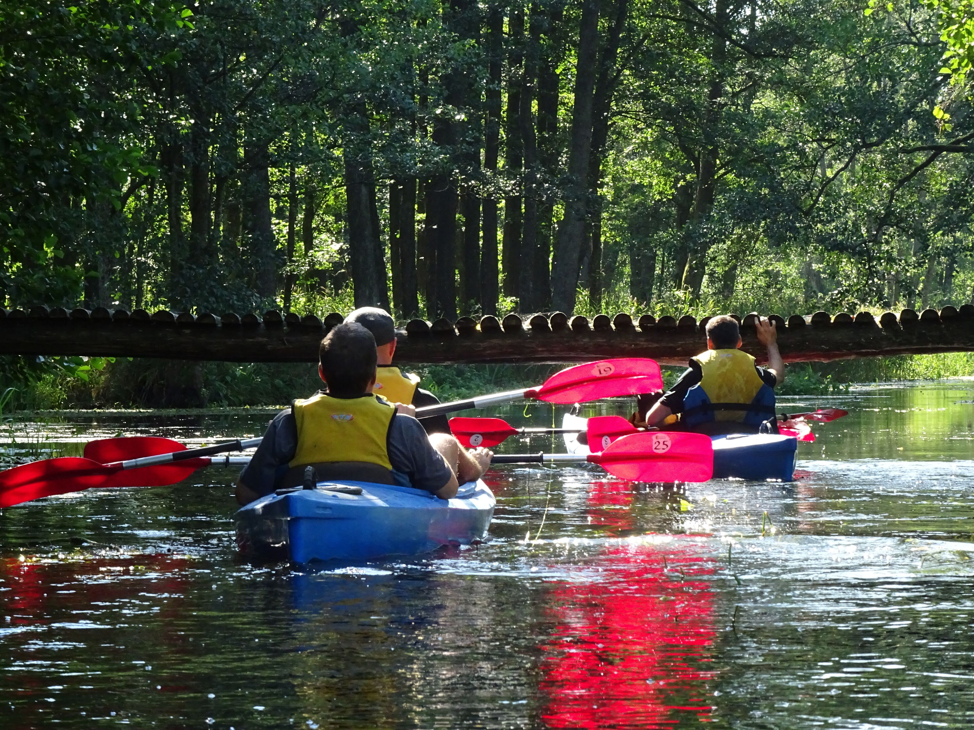 Zwei Personen in Kajaks auf einem Fluss, mit Schwimmwesten und beim Paddeln.