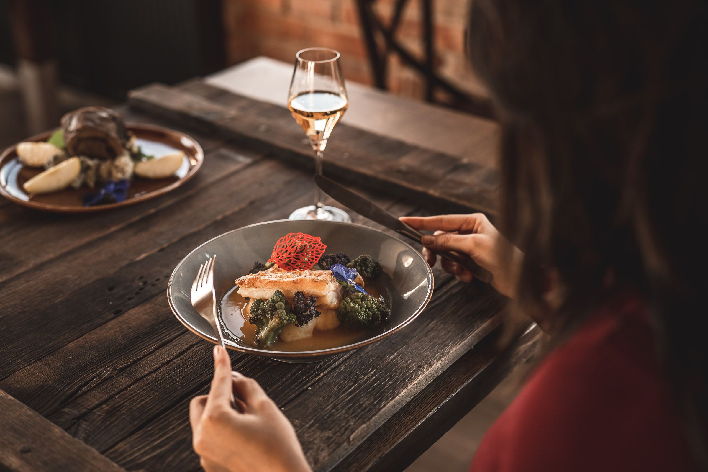 A dining table with a plate of food, a glass of white wine, and a fork.