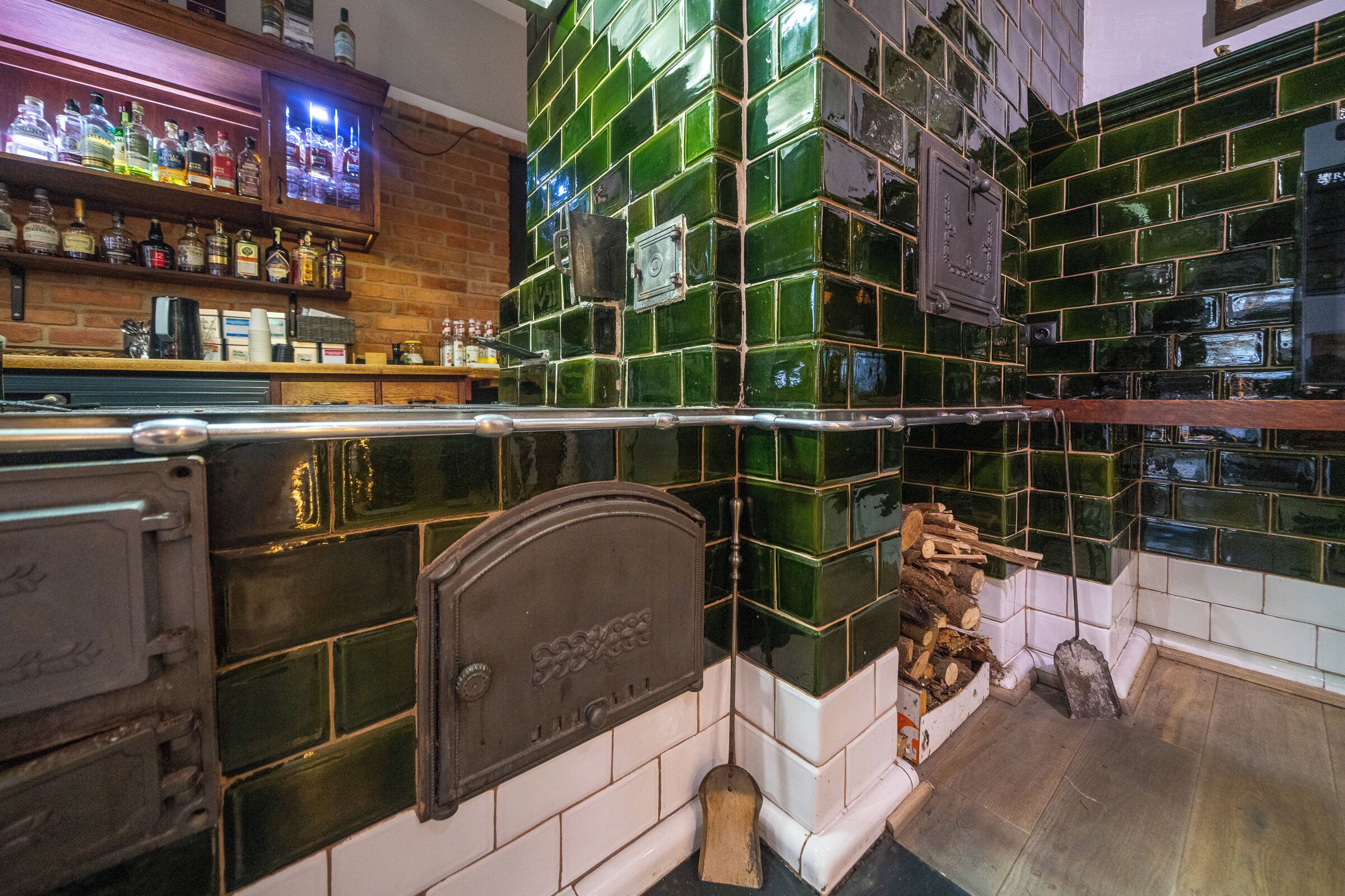 A bar area with a green-tiled backsplash, a wooden shelf with liquor bottles, and a television screen.