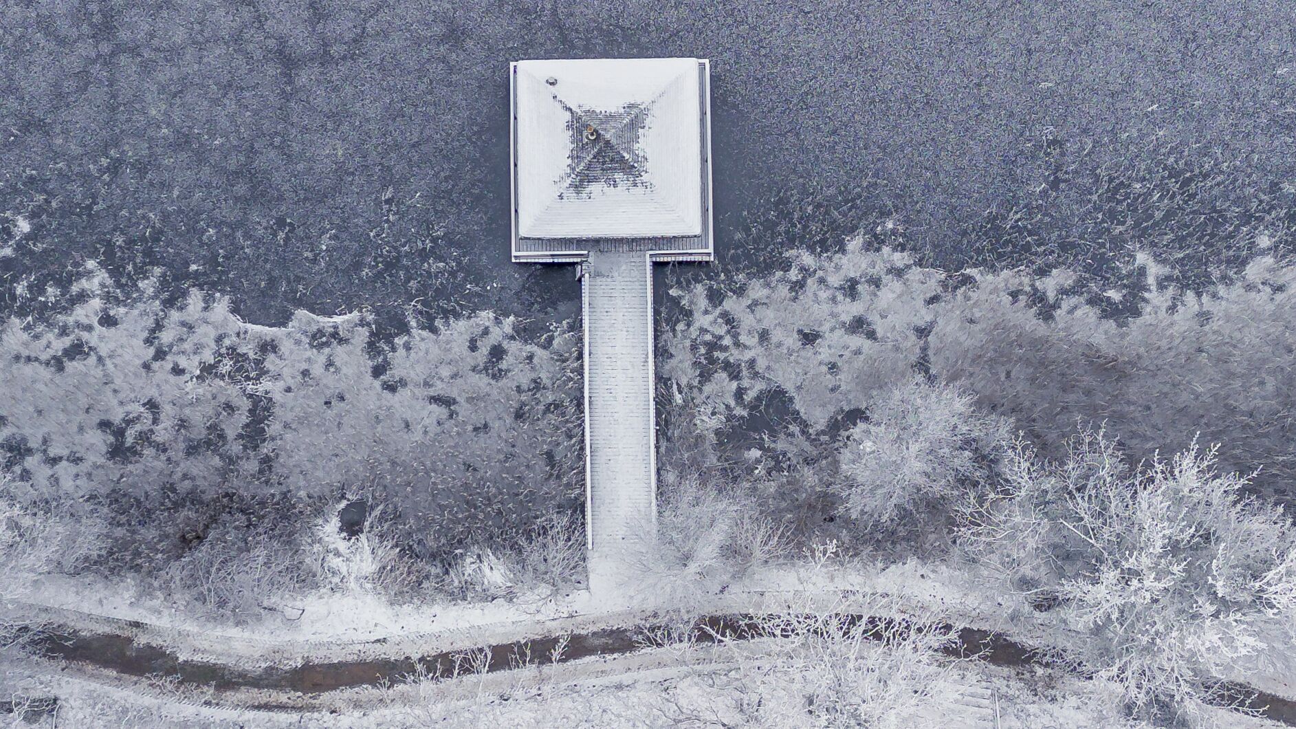 Une armoire électrique recouverte de neige, posée sur une surface en béton, avec une végétation clairsemée tout autour.