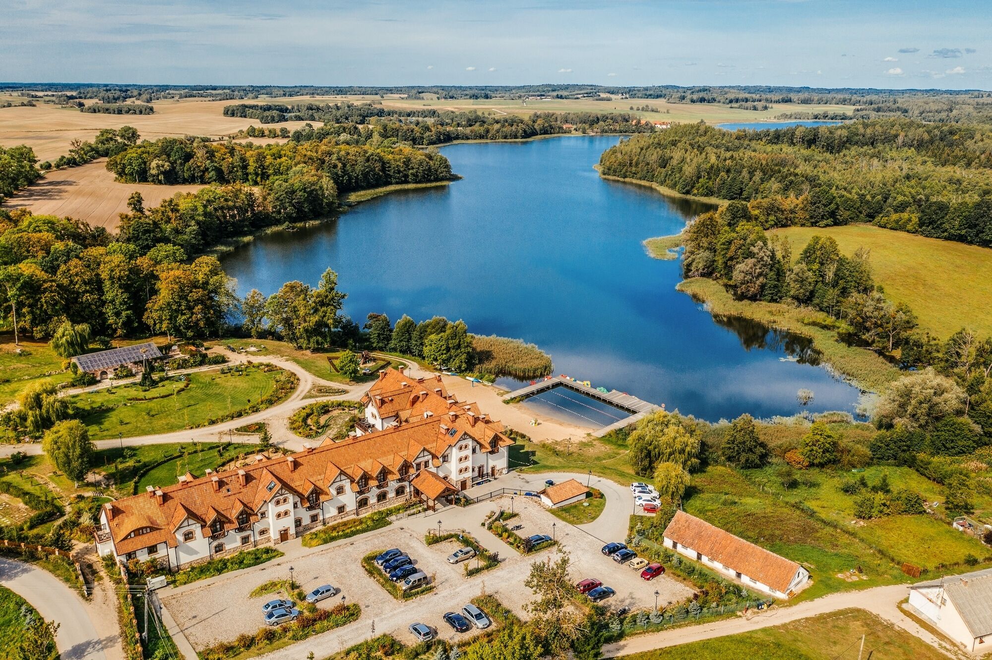 Vista aerea di una proprietà sul lago con un edificio grande, un’area parcheggio e vegetazione circostante.