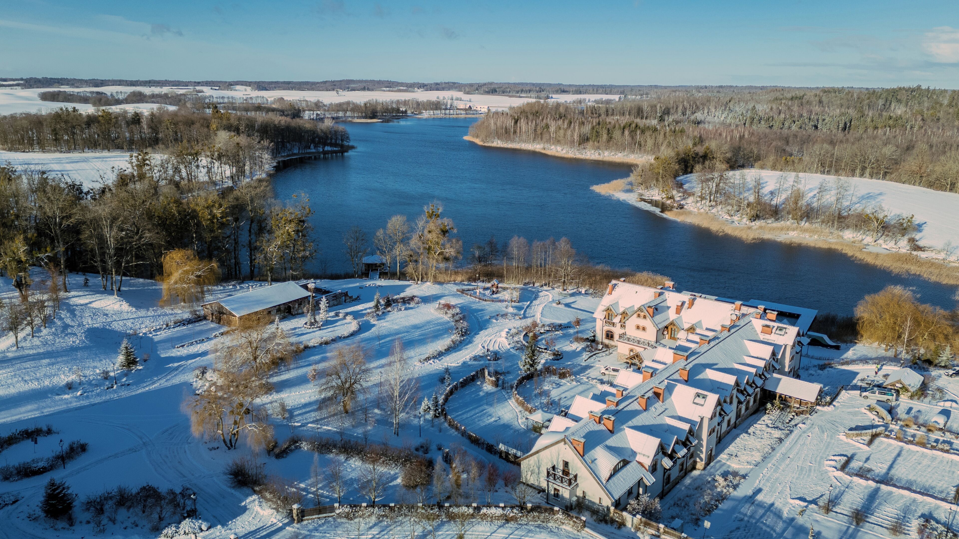 Schneebedeckte Landschaft mit Fluss, Brücke und einer Ansammlung von Gebäuden mit verschneiten Dächern.