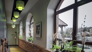 Un pasillo con pared de ladrillo, lámparas de diseño verde y plantas en macetas.