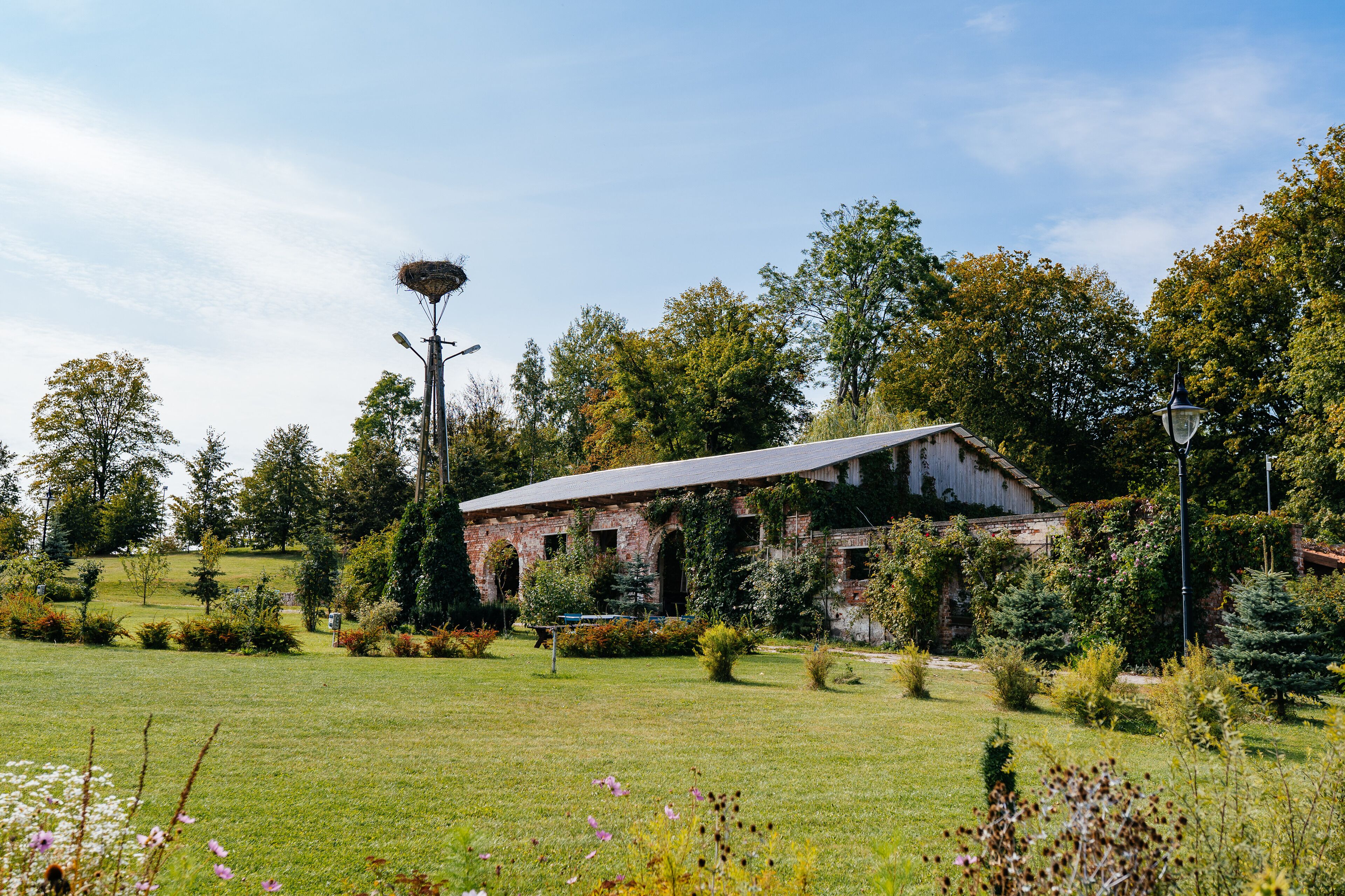 A rustic building with a sloped roof surrounded by a well-maintained garden and trees.