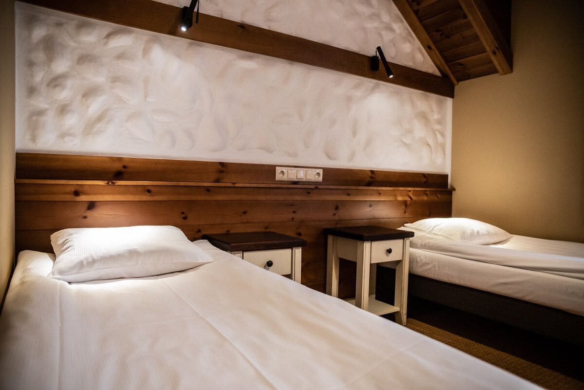 Ein Zimmer mit zwei Betten, Holz-Kopfteilen, einer Decke mit Struktur und einem kleinen Nachttisch mit Schublade.