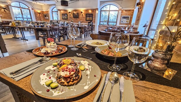 Un restaurante con varias mesas dispuestas, con platos de comida, copas de vino y cubiertos.