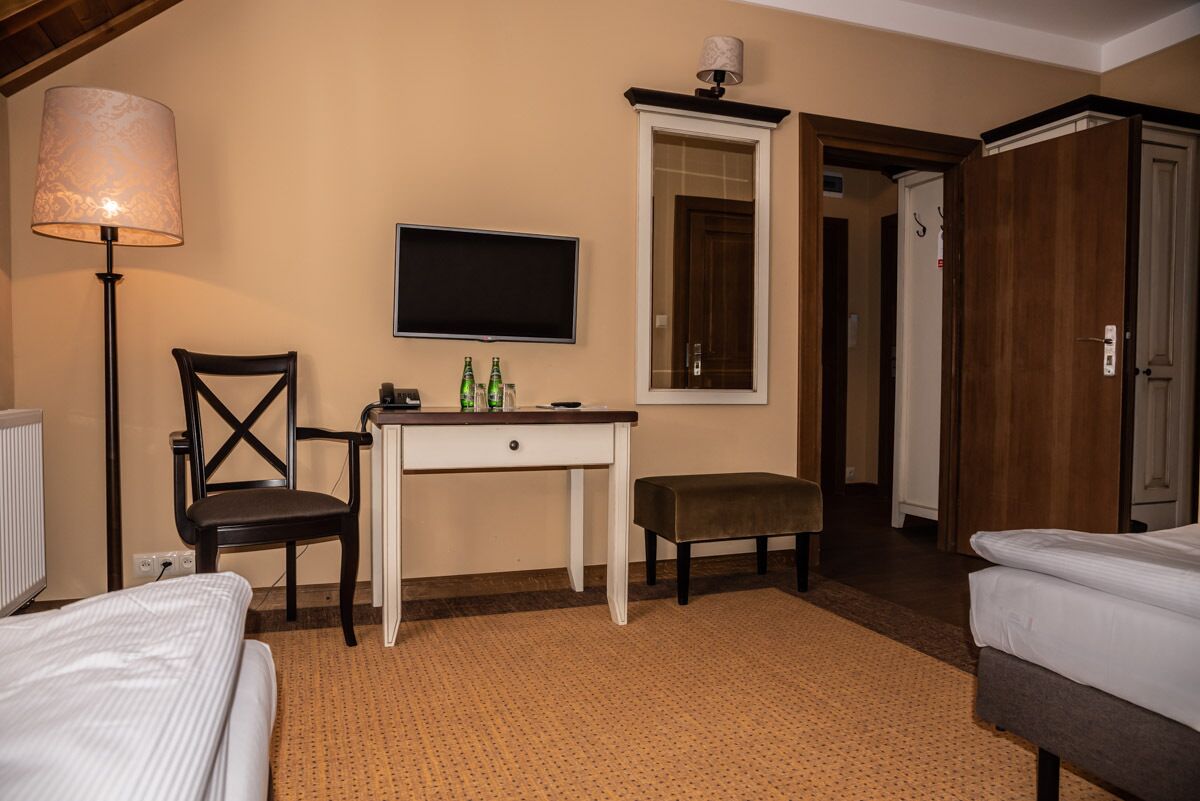 A hotel room with a bed, a desk with a chair, a television, and a door leading to another room.