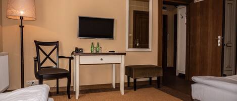 A hotel room with a bed, a desk with a chair, a television, and a door leading to another room.