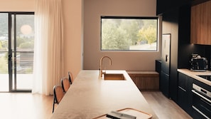 A modern kitchen with a large island, a built-in oven, and a window with a view of trees.