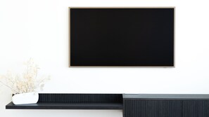 A flat-screen TV mounted on a wall above a dark wood console with a white vase containing dried flowers.