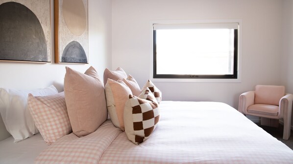 A bedroom with a bed, pillows, a chair, and a window.