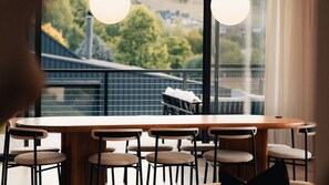 Une table ronde entourée de six chaises, avec vue sur un balcon doté d’une balustrade et un bâtiment en arrière-plan.