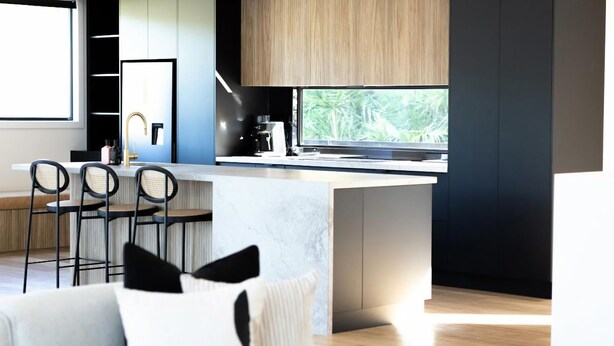 A modern kitchen with a large island, bar stools, and a view of greenery outside.