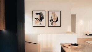 A modern interior with two abstract paintings on the wall, a minimalist white bench, and a wooden table with a tray.