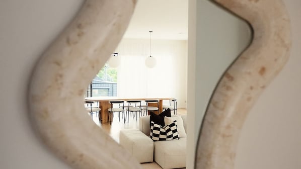 Un interior moderno con comedor, un sofá con almohadones a cuadros y un espejo grande que refleja el espacio.