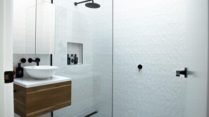 Une salle de bain moderne avec un lavabo blanc, un meuble-lavabo en bois et un espace douche aux carreaux blancs.
