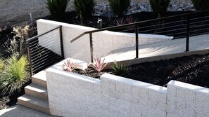 A concrete staircase with metal railings, surrounded by landscaped garden beds with various plants.