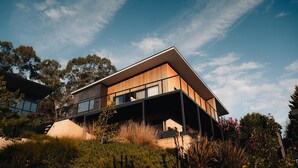 A modern two-story house with a flat roof, large windows, and a balcony.